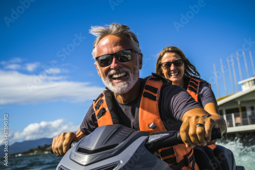 Happy smiling elderly Caucasian couple in life vests riding jet ski on a lake or along sea coast. Active senior people having fun on water scooter. Healthy lifestyle for retired persons.