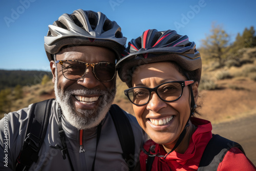 Elderly smiling couple in safety helmets riding bicycles together to stay fit and healthy. African American seniors having fun on a bike ride in autumn park. Retired people lead active lifestyle.
