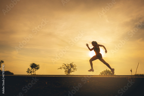 Fototapeta Naklejka Na Ścianę i Meble -  Silhouette of young woman running sprinting on road. Fit runner fitness runner during outdoor workout. Selected focus