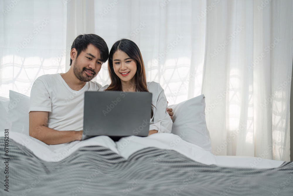 Photo of happy young couple using laptop while relaxing on bed at home. Photo of happy young couple using laptop while relaxing on bed at home.