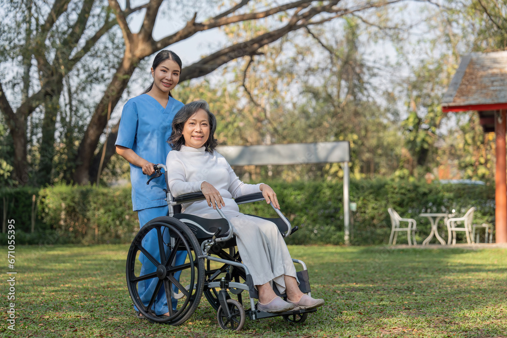 Young female in uniform with senior patient in a wheelchair chilling out in park