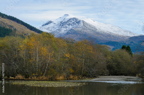 autumn-colored trees by the river and high snow-covered mountains