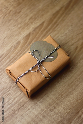 Present wrapped with recycled paper, twine and pressed eucalyptus leaf. Sustainably wrapped present, without plastic or glue. Wooden background, selective focus.