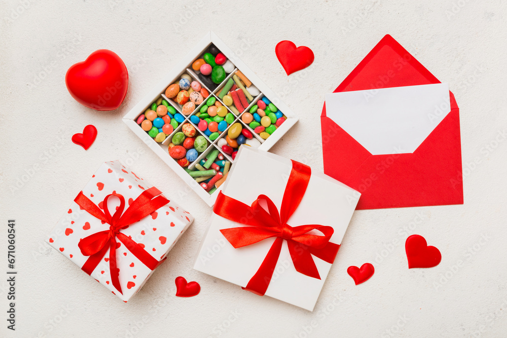 Red envelope with candy and gift box and Valentines hearts on colored background. Flat lay, top view. Romantic love letter for Holiday concept