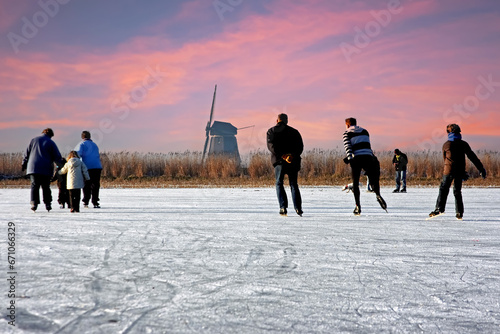 Ice skating at the windmill in the countryside from the Netherlands at sunset photo