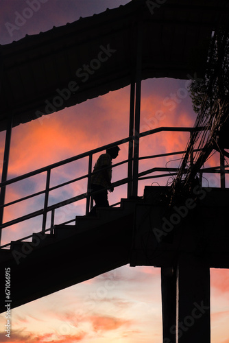 Silhouette of a foot over bridge, person claiming the stairs. Clear warm Sunset sky background.