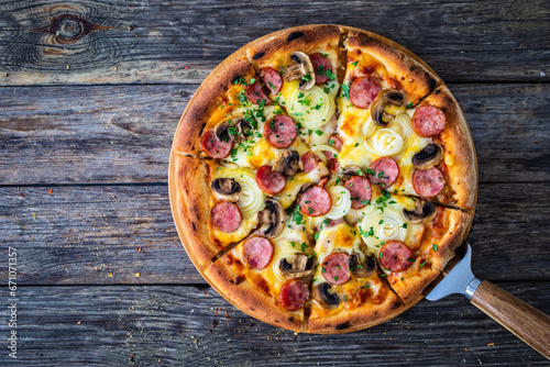 Circle pizza with sausages, onion and mozzarella cheese on wooden table 