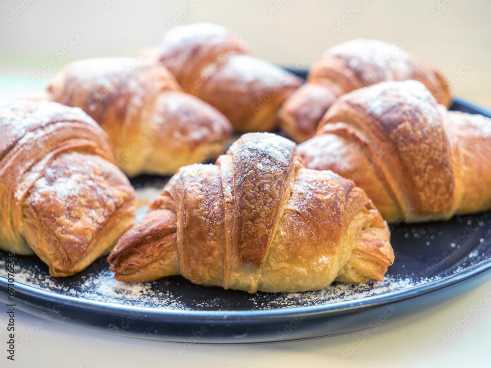Some homemade croissants on dark plate on top of a wooden tabletop, close-up.