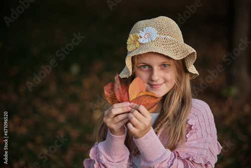 Portrait of a happy girl dressed in an autumn trendy fashion style with autumn fallen leaves in her hand isolated on an nature background.