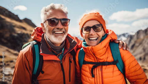 smiling senior couple in the mountains with sunglasses and backpacks on