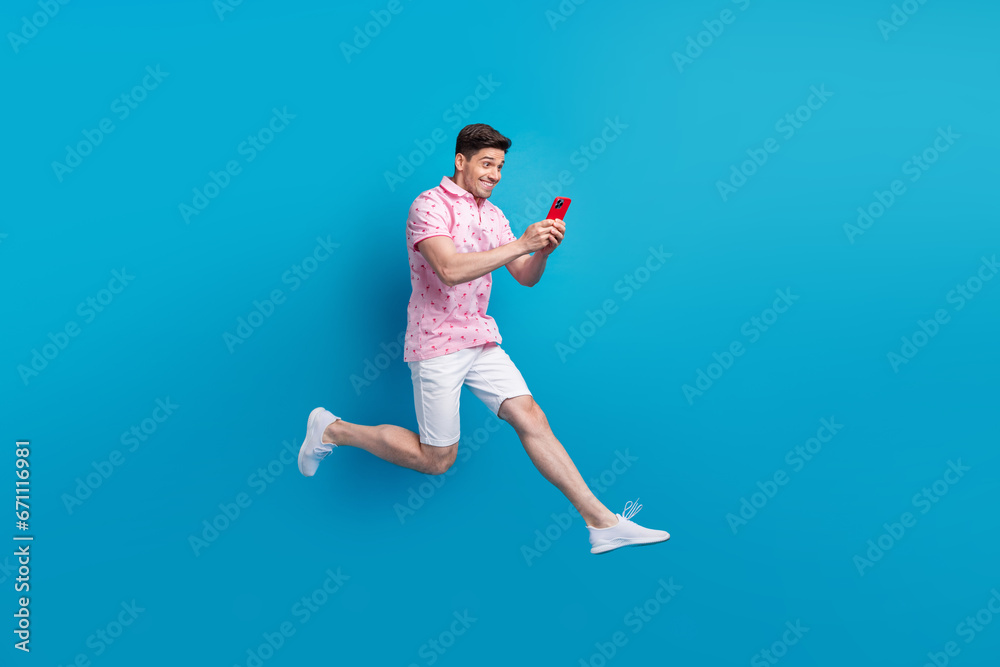 Full body profile photo of crazy cheerful man jump rush use smart phone texting isolated on blue color background Full body profile photo of crazy cheerful man jump rush use smart phone texting isolated on blue color background