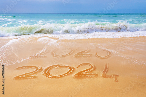 2024 written on the sand of a beach, ocean waves, travel new year greeting card photo