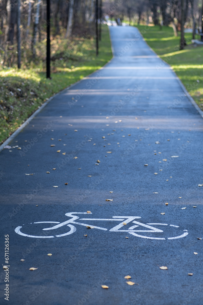 Obraz premium A signpost or bicycle road sign painted on the asphalt in a city park. Bicycle path in the forest. The concept of safety, compliance with traffic rules. Bike Lane.
