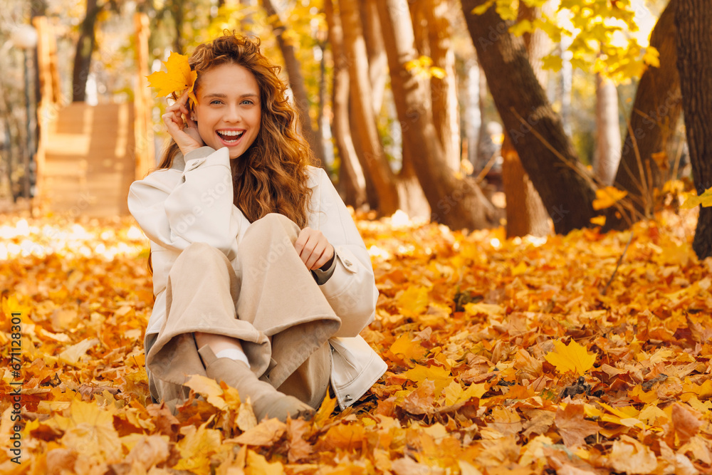 Smiling young woman sitting on the autumn foliage on the ground of the forest with the yellow leaves Smiling young woman sitting on the autumn foliage on the ground of the forest with the yellow leaves