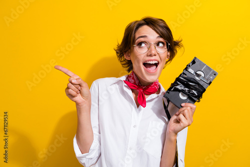 Photo of astonished cute person hold movie videocassette look direct finger empty space isolated on yellow color background photo
