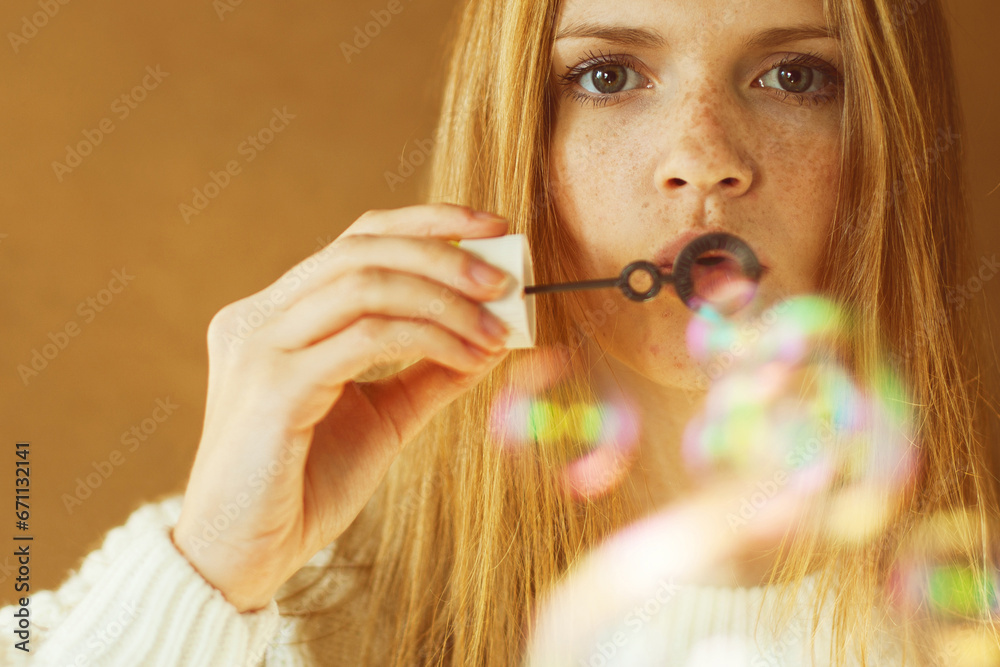 Never get old concept. Funny portrait of fashion model with long red hair in white sweater blowing party bubbles over wooden background. Daylight. Close up. Text space. Studio shot Never get old concept. Funny portrait of fashion model with long red hair in white sweater blowing party bubbles over wooden background. Daylight. Close up. Text space. Studio shot