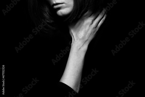 Home violence concept. Close up portrait of young woman hiding face posing with hand on neck isolated on black background. Human emotion, expression, rights, communication. Text space. Monochrome shot photo