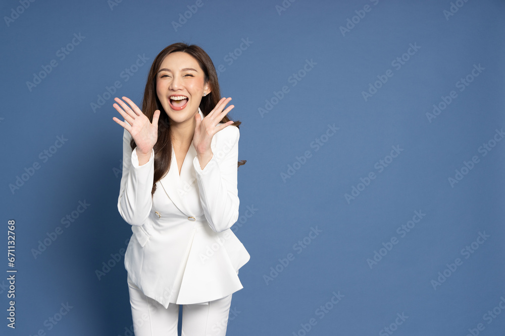 Asian business woman with open mouths raising hands screaming announcement isolated on blue background Asian business woman with open mouths raising hands screaming announcement isolated on blue background
