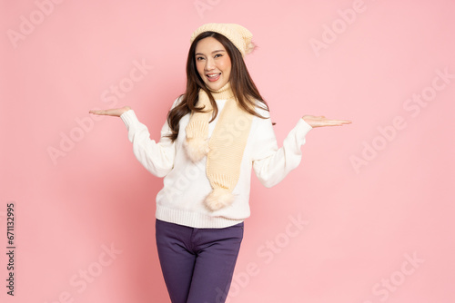 Happy young Asian woman traveler in sweater shirt smiling and presenting or showing open hand palm with copy space for product isolated on pink background