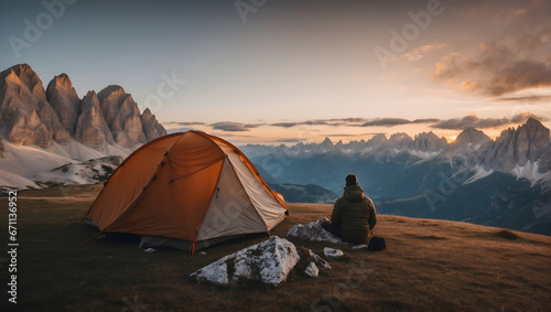 freedom concept  back view of a man sitting next to a tent on a mountain overlooking the peaks of the Dolomites in Italy before sunset