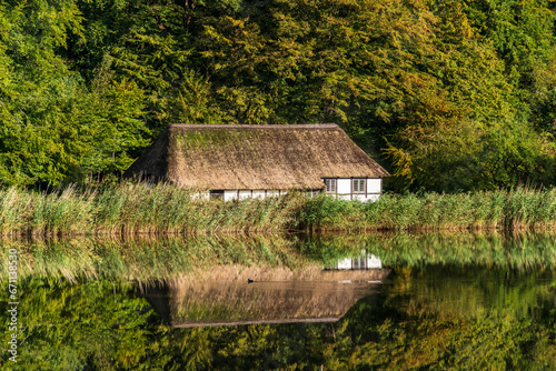Eine Reetdachkate an einem Teich im Freilichtmuseum Kiel-Molfsee mit Wasserspiegelung
