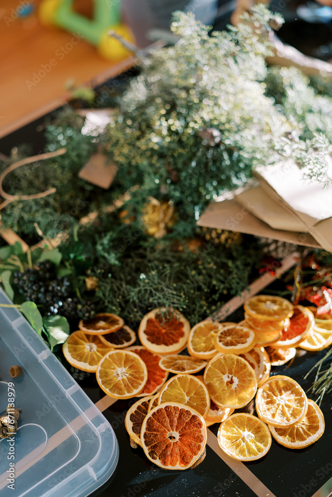 Pieces of dried orange, coniferous branches and berries for a Christmas wreath lie on the table