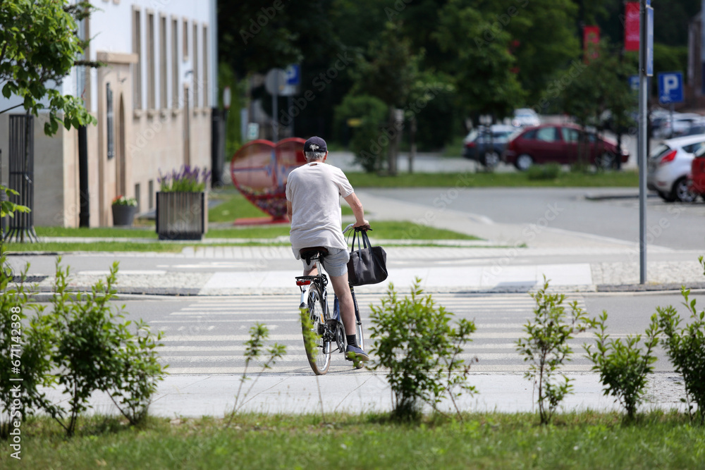 Starszy mężczyzna jedzie rowerem przez przejście dla pieszych. - obrazy, fototapety, plakaty 