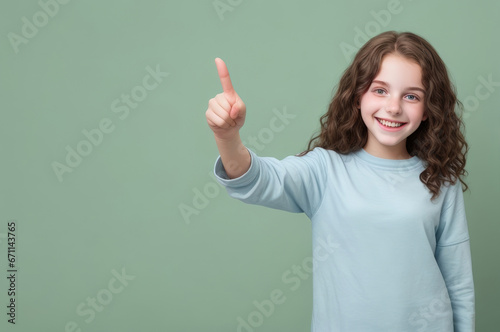 An excited young ginger girl standing alone on a green background, grinning and pointing with her index finger. Copy space for text, advertising, message, logo