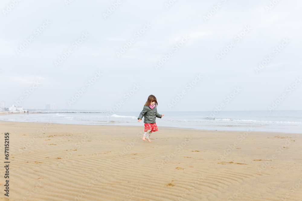 running small girl in winter clothes on the sand beach