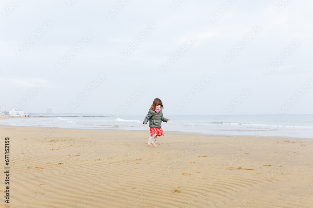 running small girl in winter clothes on the sand beach running small girl in winter clothes on the sand beach
