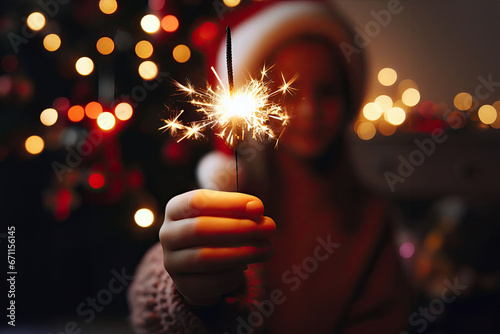 girl in Santa Claus hat holding a Christmas sparkler in a living room with Christmas decorations