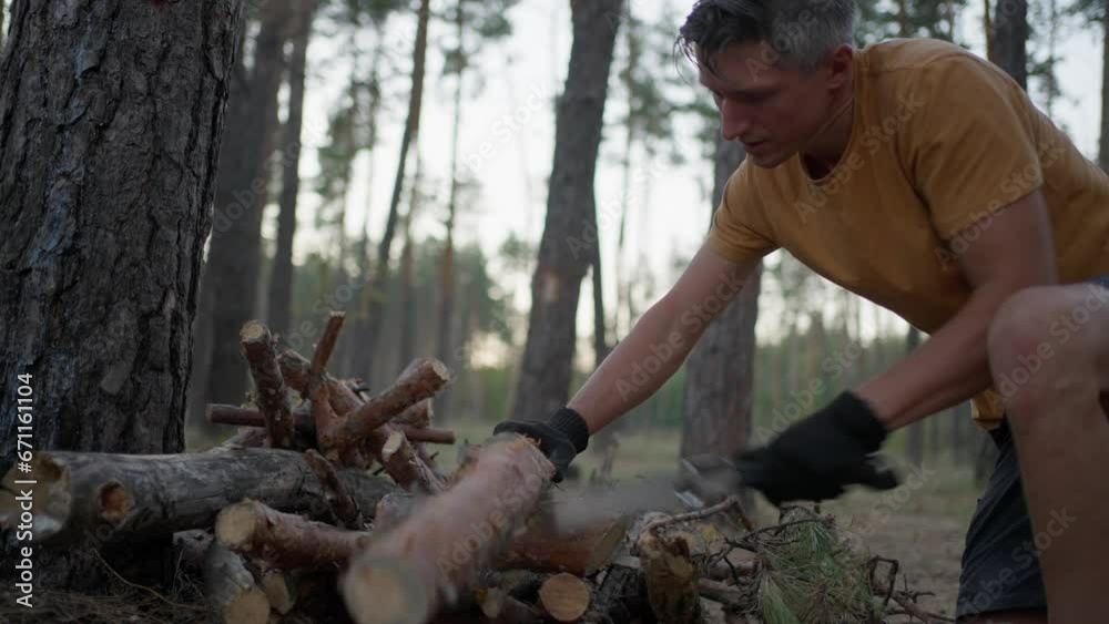 male tourist cuts log with hand saw in evening in forest. traveler preparing firewood for campfire. man in wild. hiker outdoors surviving in wild nature, making fire male tourist cuts log with hand saw in evening in forest. traveler preparing firewood for campfire. man in wild. hiker outdoors surviving in wild nature, making fire