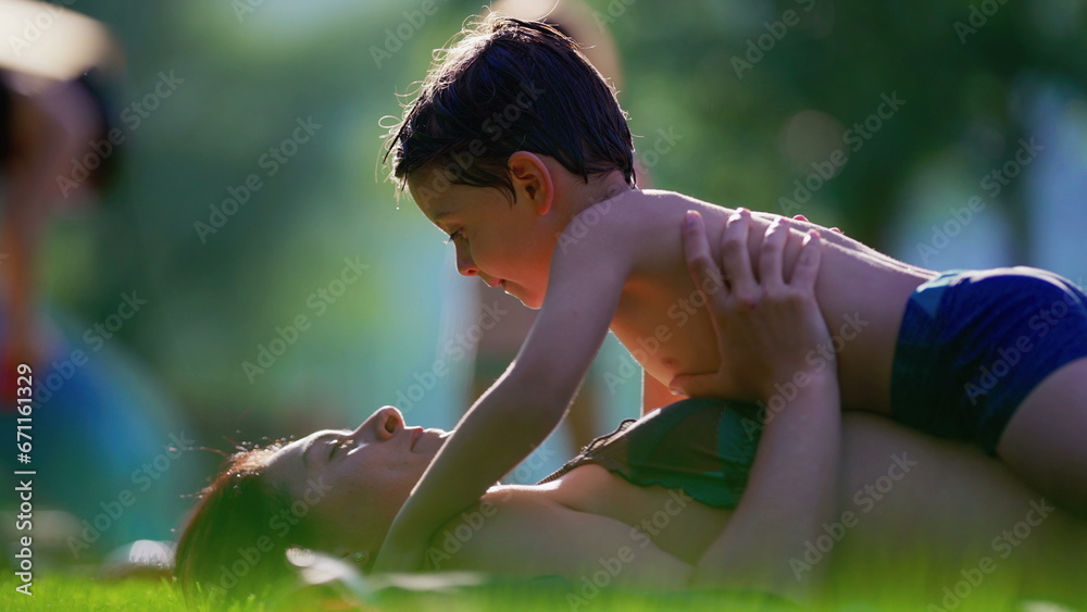 Candid child and mother laid on grass during summer day after swimming at the pool. Warm tender moment between parent and little boy Candid child and mother laid on grass during summer day after swimming at the pool. Warm tender moment between parent and little boy
