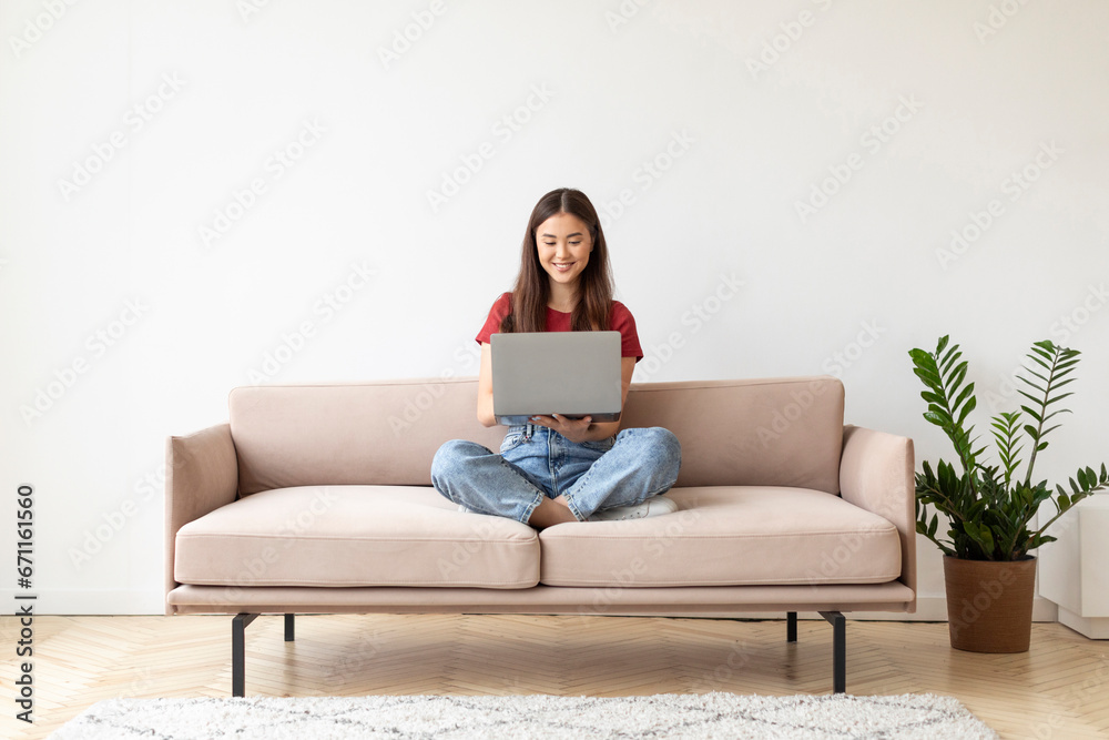 Beautiful Young Asian Woman Using Laptop While Sitting On Couch At Home