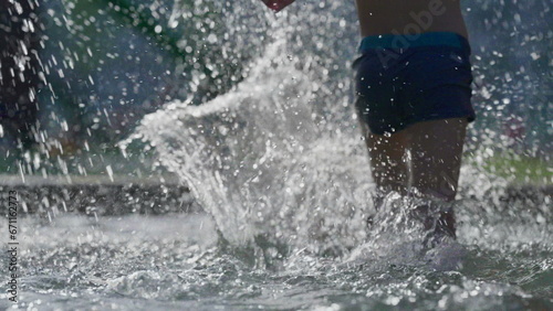 Child stepping into water by poolside and sprinting in slow-motion splashing water droplets everywhere in 120fps. Kid having fun at swimming pool during hot summer day