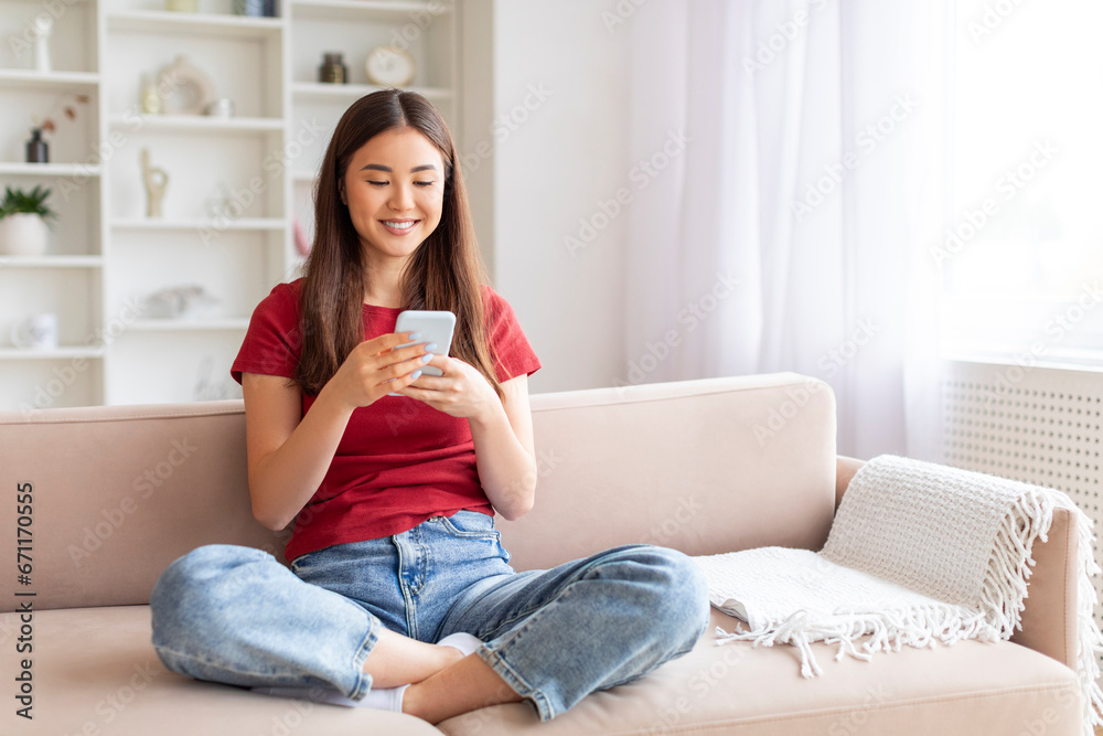 Smiling Young Asian Woman With Smartphone Relaxing On Couch At Home Smiling Young Asian Woman With Smartphone Relaxing On Couch At Home
