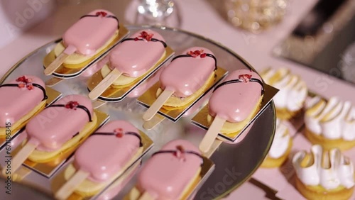 Festive candy bar. Close up of sweet buffet with yummy cakesicles in pink glaze, decorated sublimated strawberries on mirror plate. Tasty dessert, close-up, delicious. Celebration event catering.