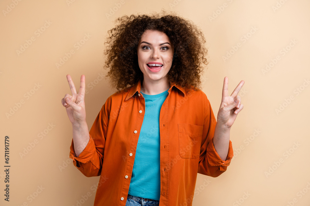 Photo portrait of lovely young lady excited impressed show v-sign wear trendy orange garment isolated on beige color background