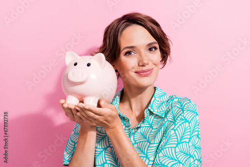 Portrait of pretty positive young girl arms hold money savings bank pig isolated on pink color background