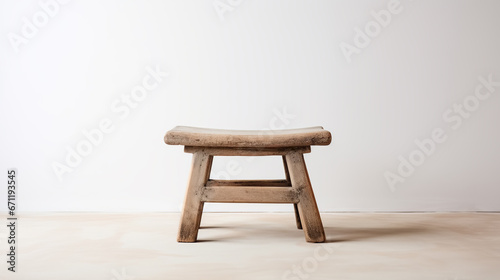 Old low Chinese wooden stool in an empty room with white wall and floor. Traditional craft, handmade furniture. Copy space. photo