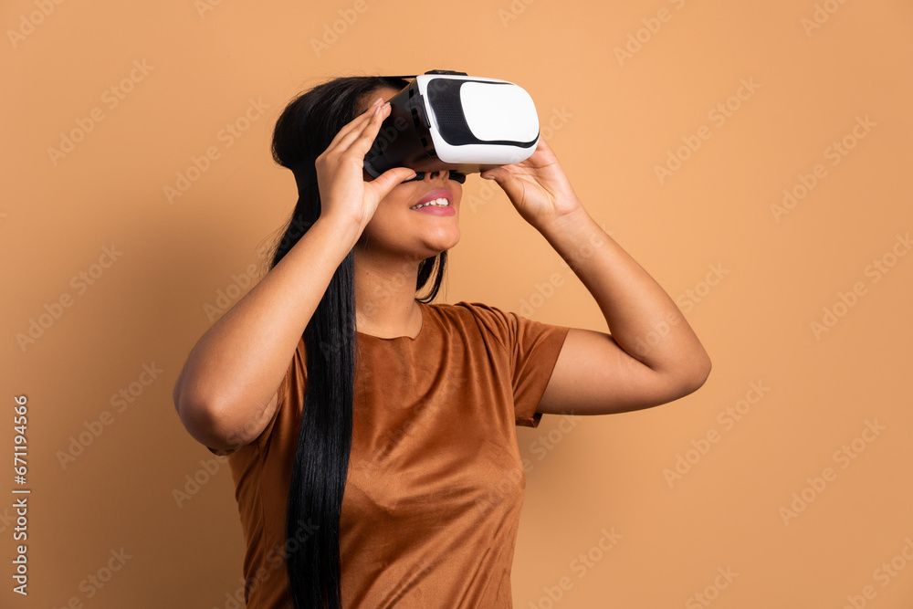 joyful afro brazilian woman Using VR headset and gesturing in beige studio background. virtual reality, technology simulation concept. joyful afro brazilian woman Using VR headset and gesturing in beige studio background. virtual reality, technology simulation concept.
