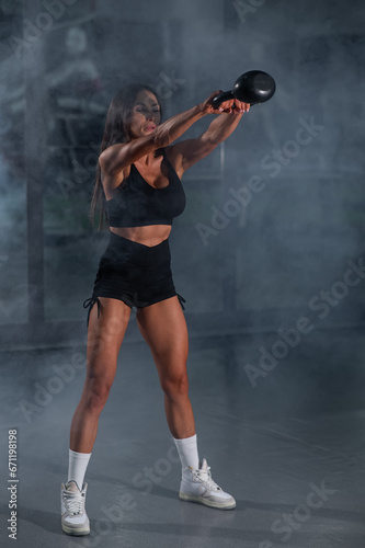 A beautiful brunette with big breasts does Russian swings with a kettlebell. Vertical photo. 