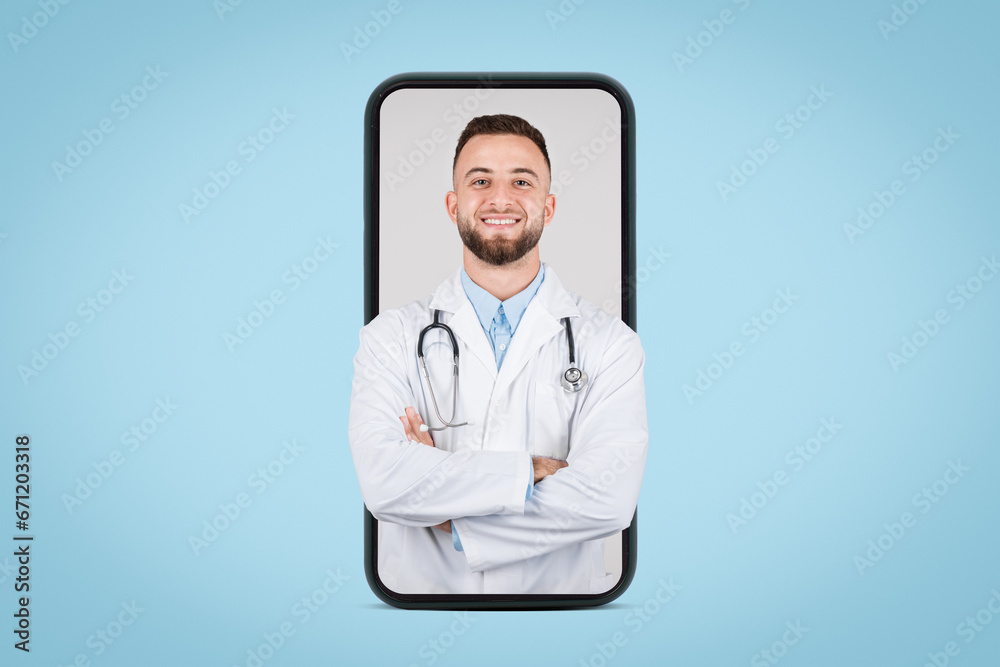 Fototapeta premium Smiling young male doc on phone screen, blue backdrop