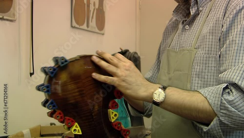 A Violin Maker Repairing a Violin in Violin Repair Workshop, Craftsman Holding Violin with Clamps during Restoration Work. Close Up.