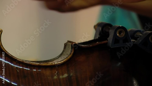 A Man Repairing a Violin in Violin Repair Workshop, Craftsman Holding Violin with Clamps during Restoration Work. Close Up.