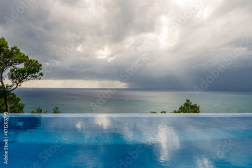 Un ciel menaçant domine un océan calme et serein, avec une subtile piscine à débordement au premier plan et une lointaine petite tornade.