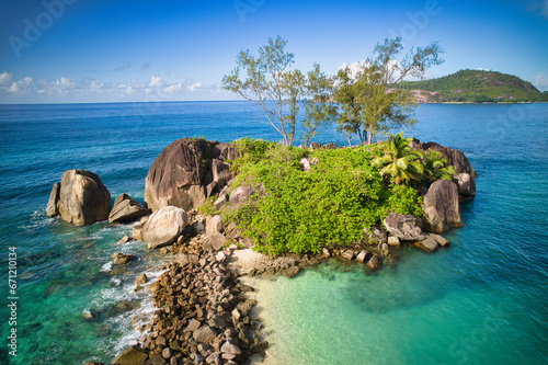 Drone of Therese island in the horizon behind granite rocks and trees, Mahe Seychelles 