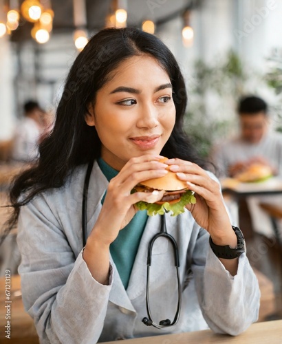 Asian female doctor eating burger at restaurant