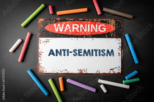 Anti-Semitism. Metal warning sign and colored pieces of chalk on a dark chalkboard background photo