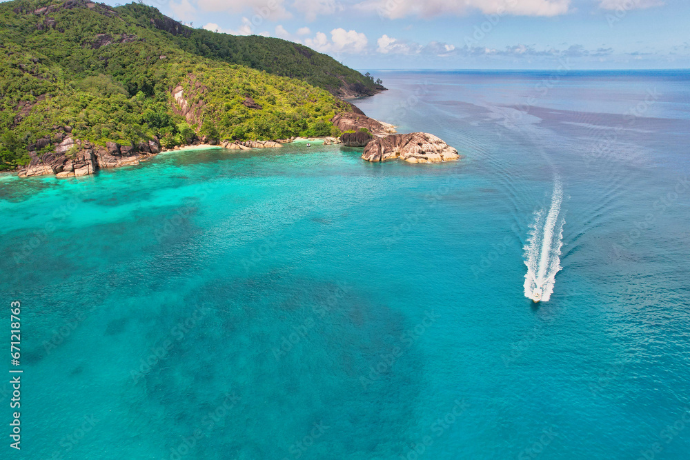Drone shot of Anse du riz, rice beach beach, transparent sea, lush forest and granite stones, docked and passing boat 1